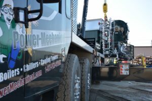 Industrial service truck with pipes and a mural, branded Power Mechanical, at an industrial site. 
