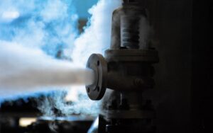 Industrial valve releasing a jet of white steam through a pipe in a dim setting. 