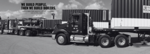Black-and-white industrial scene with a large semi-truck and equipment; headline reads 'We build people, then we build boilers.'