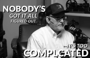 Man wearing a cap, headset, and glasses speaking into a microphone in a studio; bold overlay reads “NOBODY'S GOT IT ALL FIGURED OUT” and “IT'S TOO COMPLICATED.”