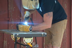 Welder in protective gear welding metal on a worktable, sparks flying.