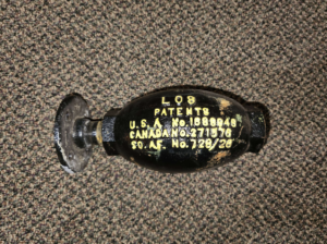 Old black grenade-like device with yellow patent numbers stamped on its side, on a carpet.