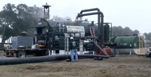 Mobile boiler plant on a truck with large hoses laid out on the ground and a worker in a hard hat nearby.