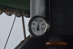 Round temperature gauge mounted on a dark metal pillar, needle near 320°C on a white dial marked °C