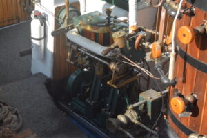 Vintage marine engine with brass fittings and a green frame in a wooden engine room aboard a vessel