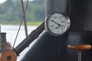 Round dial thermometer gauge mounted on a dark industrial boiler, displaying temperature on a white face.