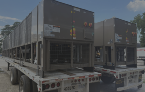 Two large industrial HVAC units on flatbed trailers outdoors, ready for transport and loading site visible in the background.