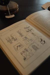 Open book with technical diagrams on a dark desk, a lamp and sticky notes nearby.