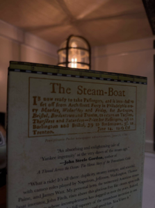 Vintage pamphlet about a steam-boat, photographed indoors with a lantern in the background. The heading reads 'The Steam-Boat' with old-fashioned text.