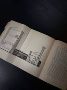Open book showing a black-and-white diagram of a boiler house with pipes on the left page and text on the right page.