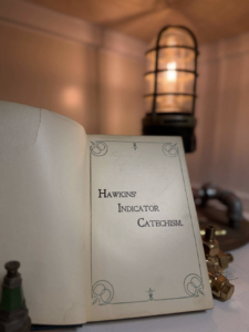 Open book showing the title 'Hawkins' Indicator Catechism' with a decorative border; a warm lantern-lit background adds ambience.