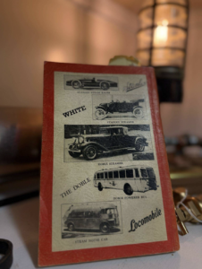 Vintage brochure page with black-and-white drawings of early cars and a bus inside a red frame.