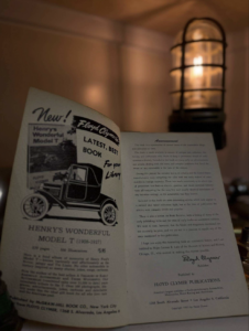 Open vintage book featuring a black-and-white illustration of an antique car with a warm lamp-lit background, conveying a retro ad feel.