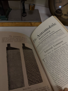 Open vintage issue of The Automobile Magazine showing pages with a two-panel illustration and editorial text on a desk.