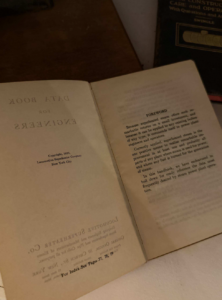 Open old, yellowed book spread on a wooden surface; right page shows a Foreword paragraph, left page has faint reversed title and copyright text.