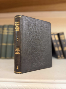 Vintage black textured hardcover titled 'Engineers Mechanical Guide' standing upright on a shelf, with other books blurred in the background.