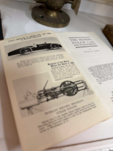 Open magazine spread featuring vintage steam car illustrations and old automotive text, with a brass scientific instrument in the background.