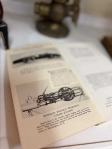 Open book showing a black-and-white illustration of a steam engine with the caption 'World's Record-Breaking Steam Engine' on the page, among columns of text.