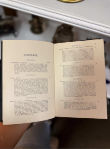 Open book showing 'Contents' pages with sections and page numbers, held on a person's lap in a cozy setting.