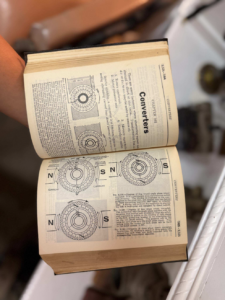 Open engineering textbook showing circular rotor/coil diagrams with N and S labels on cream pages