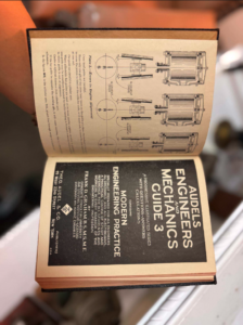Open vintage technical book showing mechanical diagrams on the top page and a dark title page reading 'Engineering Practice' on bottom.