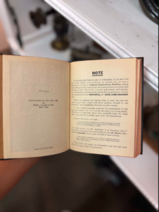 Open vintage book held in a hand, left page with copyright info and right page labeled NOTE with dense text.
