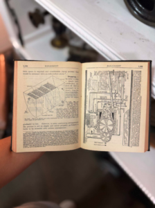 Open vintage technical book showing two pages of diagrams (machine components and piping), held by a hand.