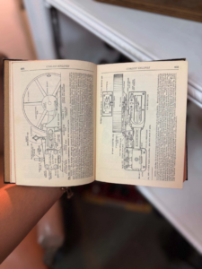 Open vintage Corliss engines manual showing detailed diagrams of engine components held by a person's arm.