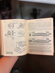 Open book with technical diagrams of Corliss engines, showing piston parts on the left page and steam valve diagrams on the right, held by a person's hand.