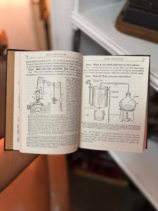 Open vintage science book showing a diagram of an engine and condenser, held by a person in a home setting.