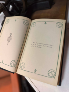 Open book opened to left and right pages with green scrollwork borders; a small emblem is visible on the left page.
