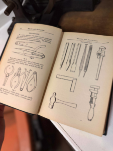Open instruction manual showing black-and-white diagrams of hand tools (pliers, pincers, calipers) across two pages, with a hammer and chisels on the right page, held by a person.