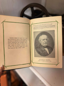 Open book showing a quote on the left page and a portrait of Matthias W. Baldwin on the right page, framed with green borders.