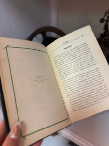 Person holds an open book, showing the preface page on the right and a blank bordered page on the left.