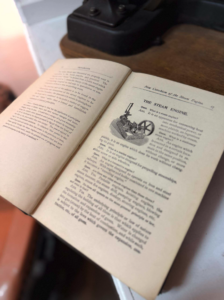 Open vintage book showing a detailed illustration of a steam engine with text on the page titled 'The Steam Engine'.
