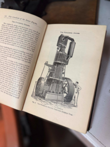 Open book with a detailed illustration of a tall steam engine labeled 'The Fitchburg Engine' and a man standing beside it for scale.