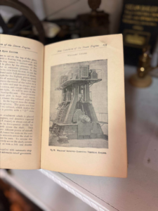 Open vintage book showing a black-and-white illustration of a vertical steam engine, captioned “William’s Improved Compound Vertical Engine.”