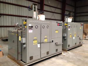 Industrial electrical switchgear cabinets with gauges and warning labels in a warehouse setting.