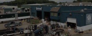 Wide view of a blue industrial repair shop with a 'Got Steam?' sign, surrounded by trucks, trailers, and heavy equipment in a busy yard.