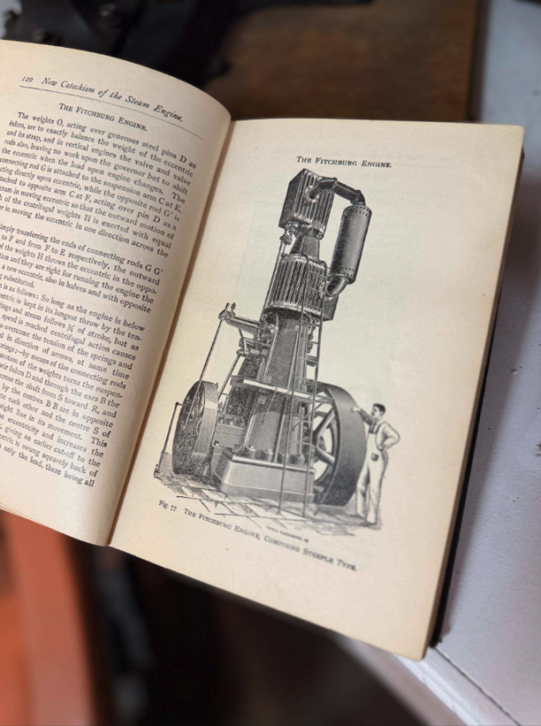 Open book with a detailed illustration of a tall steam engine labeled 'The Fitchburg Engine' and a man standing beside it for scale.