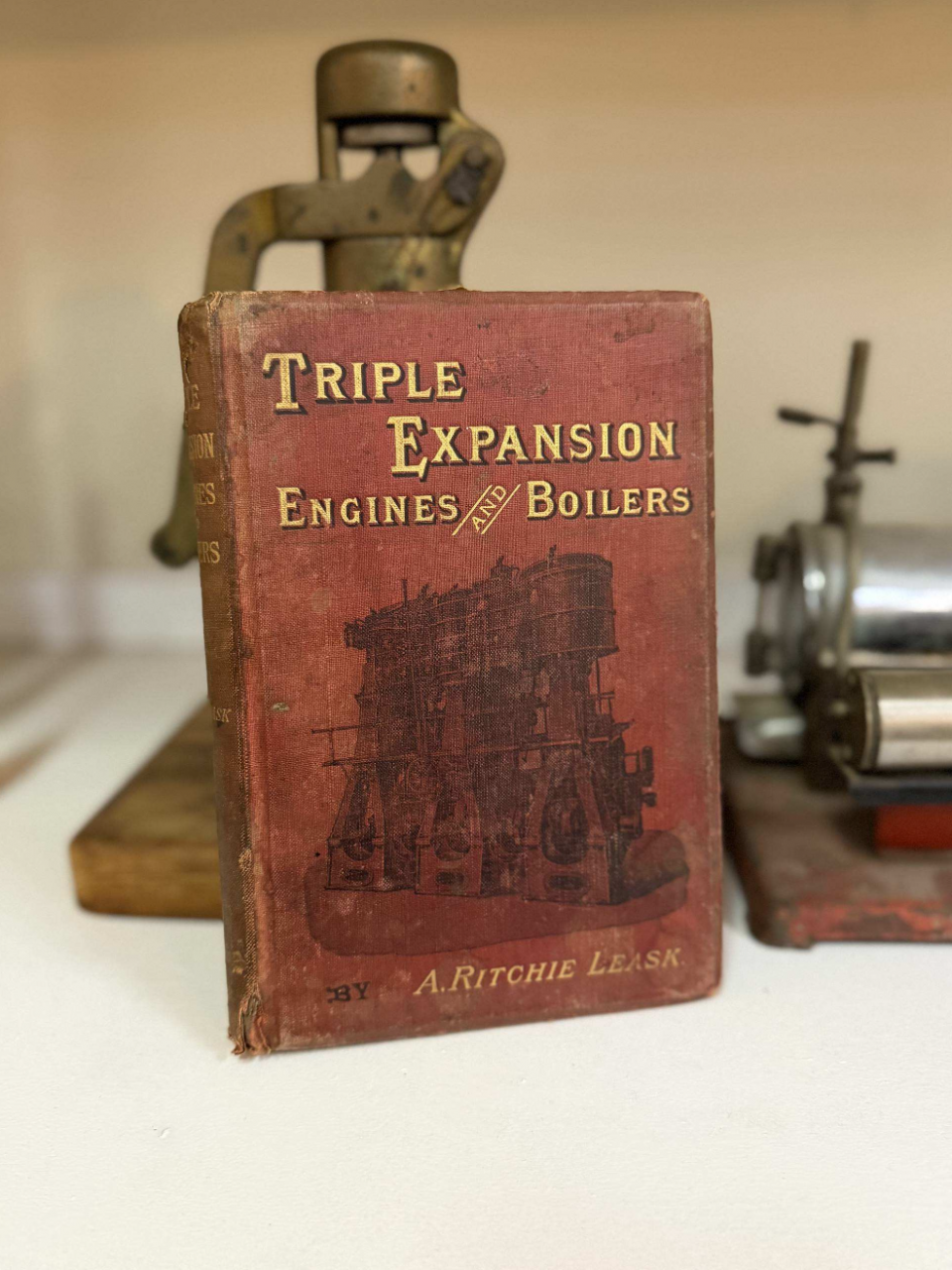 Old red hardcover book titled 'Triple Expansion Engines and Boilers' by A. Ritchie Leask, with vintage engine parts in the background.