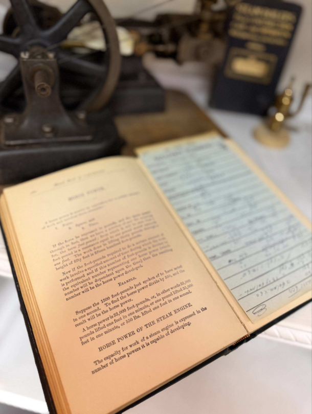 Open book on a desk, page titled 'Horse Power of the Steam Engine', with a blurred vintage machine in the background.