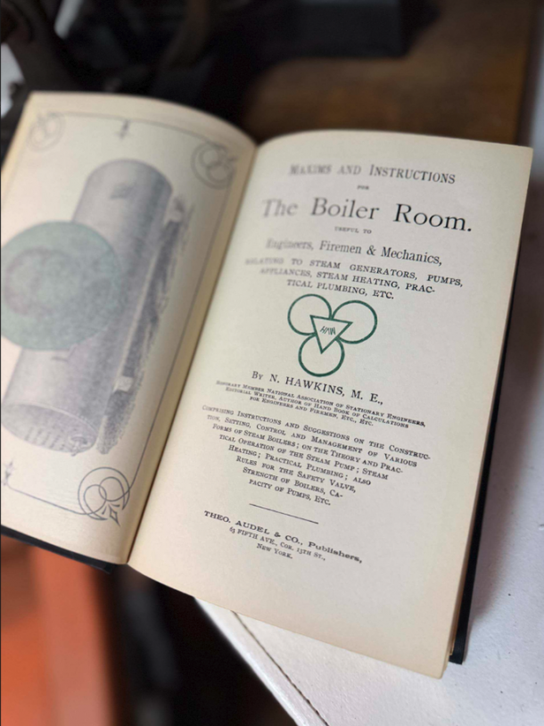 Open antique book showing the title page reading 'The Boiler Room' with decorative emblem and vintage typography on cream pages, left page has an illustration edge.
