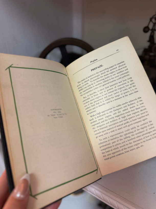 Person holds an open book, showing the preface page on the right and a blank bordered page on the left.