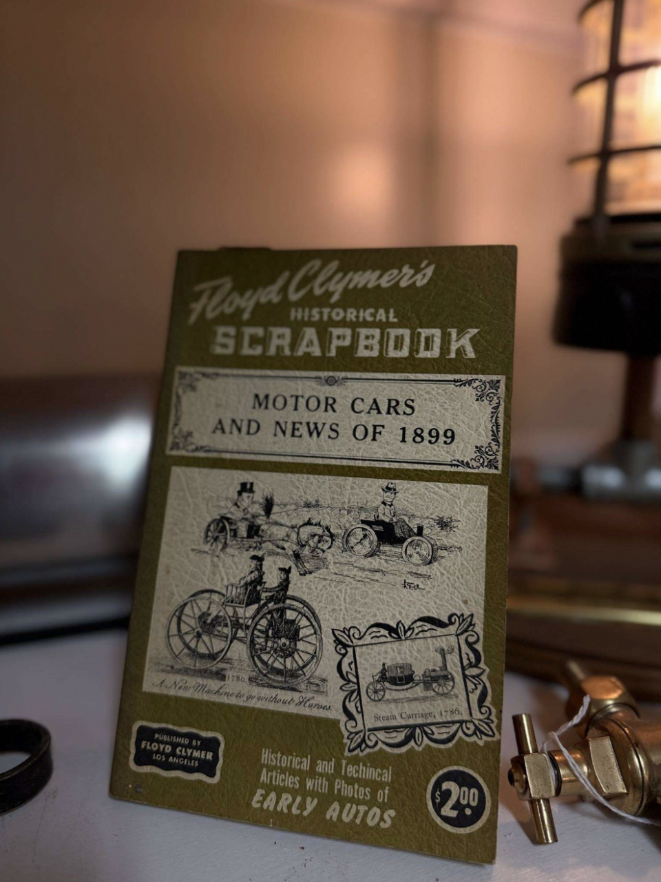 Vintage booklet titled Floyd Clymer's Historical Scrapbook with 'Motor Cars and News of 1899' and old car illustrations on the cover