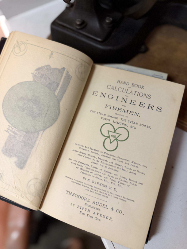 Open vintage engineering book titled 'Hand Book of Calculations for Engineers and Firemen' with decorative illustrations and a green emblem on the title page and left page edge visible in the background.