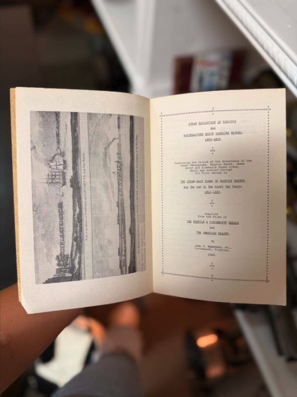 Open book held in one hand; left page has a grayscale illustration, right page shows a dotted-border title page about steamboat navigation in Virginia (antique book).