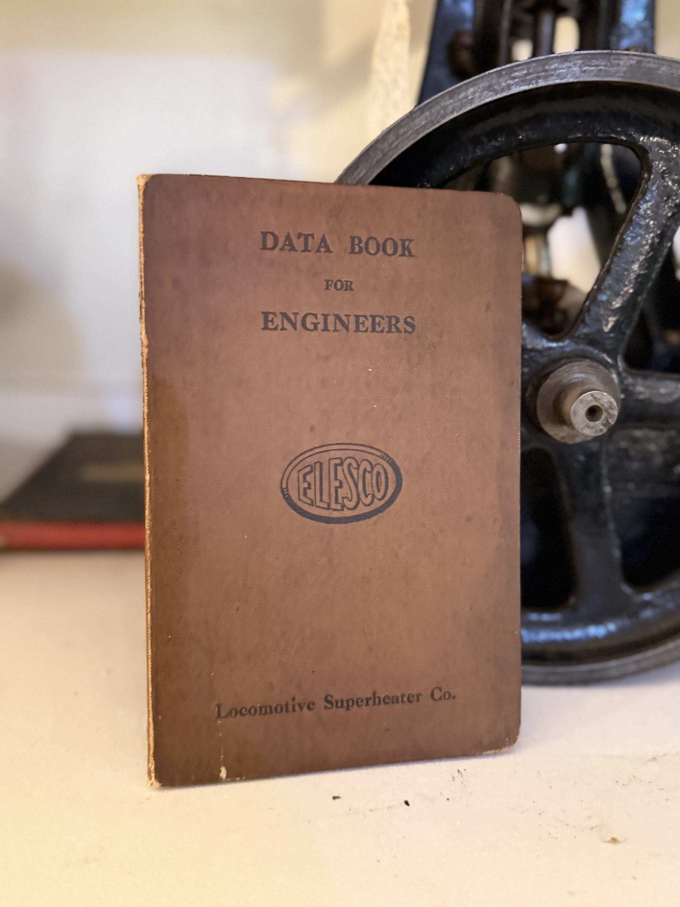Vintage brown data book titled 'Data Book for Engineers' with a logo, beside a metal wheel (Locomotive Superheater Co.).